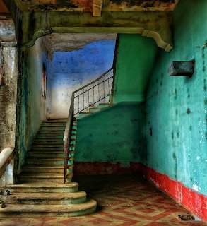 Curved wooden staircase in abandoned building with peeling turquoise walls and red trim