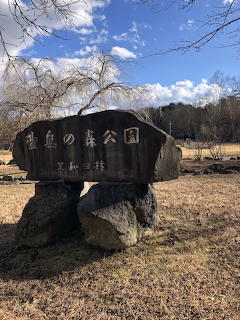 Wooden park sign with Japanese text mounted on rocks in a winter park setting with bare trees