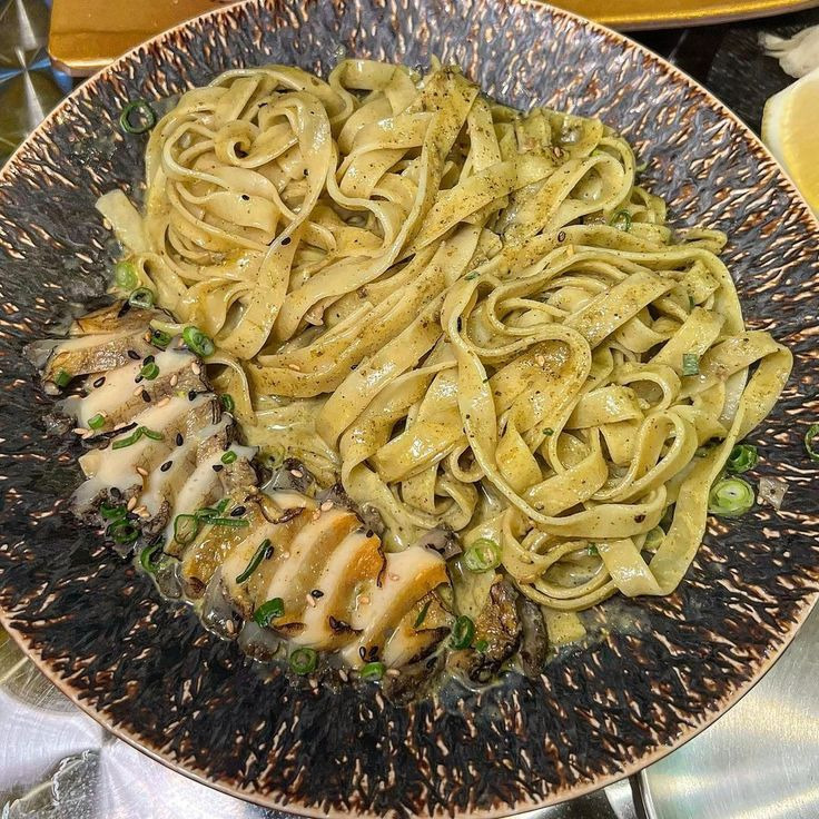 Plate of fettuccine pasta with abalone slices, green onions, and sesame seeds on a speckled dark plate