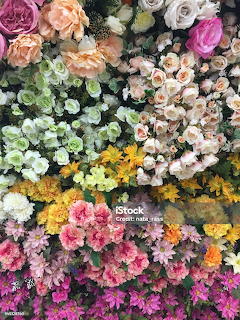 Dense wall of colorful flowers including pink roses, white hydrangeas, yellow daisies, and green foliage