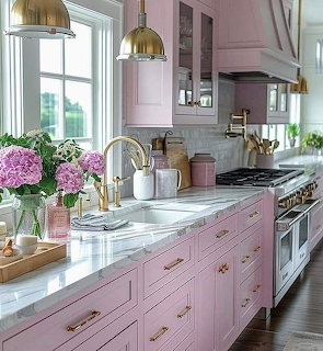 Modern kitchen with pink cabinetry, marble counters, brass fixtures, and purple hydrangeas
