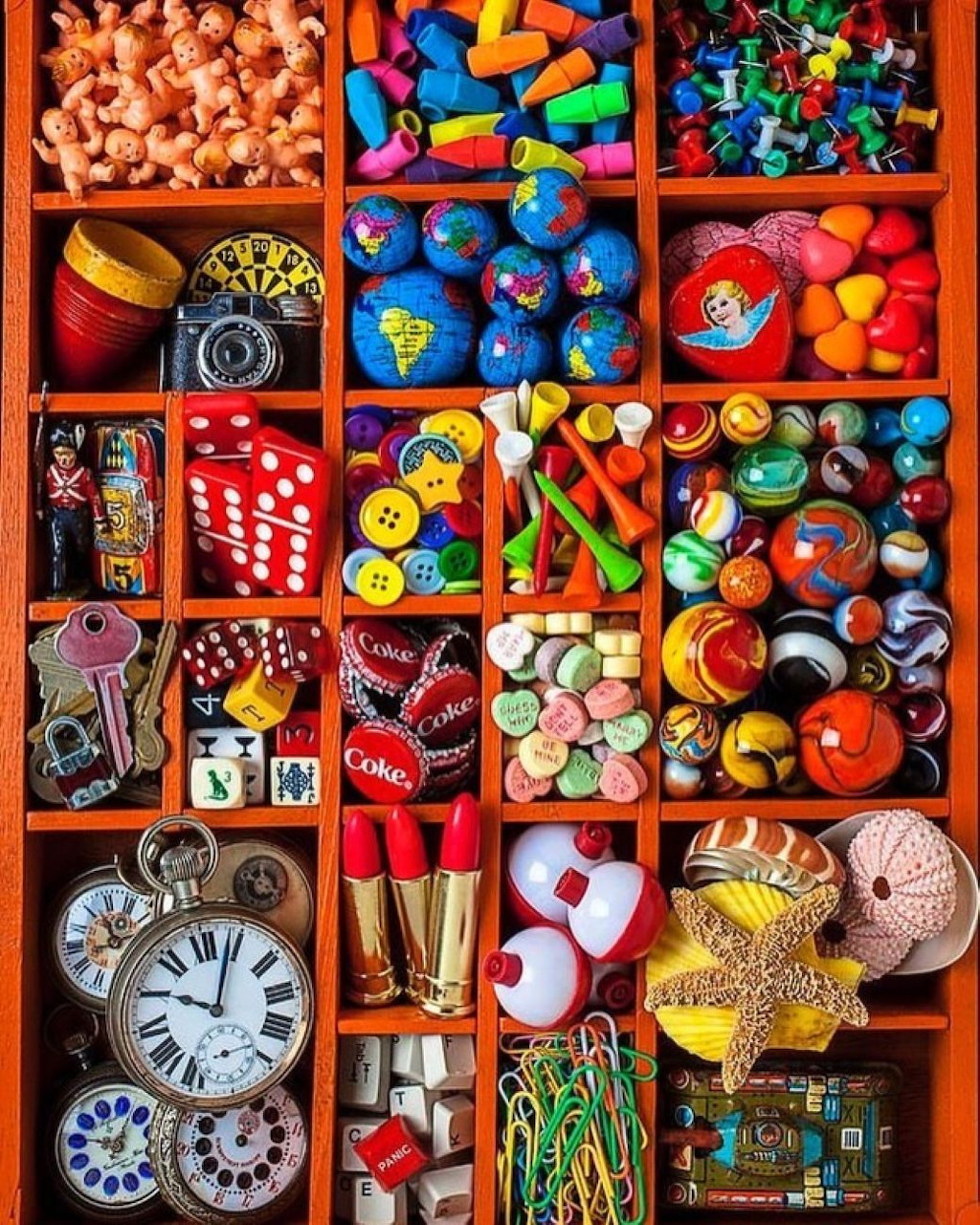 Wooden compartment tray filled with colorful assorted objects: dice, buttons, marbles, toys, keys, and paper clips