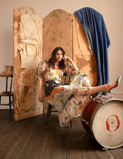 Woman in floral dress posing on a chair with feet on a drum in front of a vintage folding screen