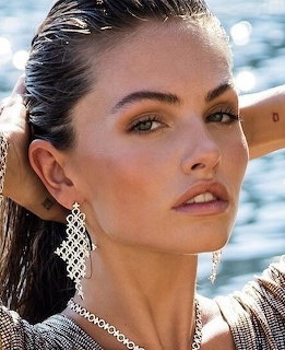 Portrait of woman with dark hair, elegant earrings, and natural makeup by the ocean