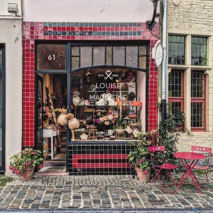 Vintage shop with red tiled storefront, window display, flowers, and cobblestone street