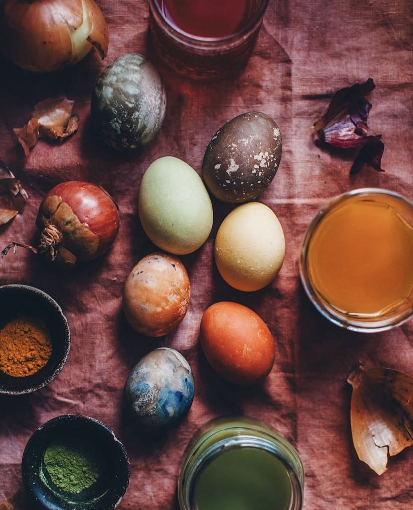 Naturally dyed Easter eggs with bowls of turmeric, matcha, and liquid dyes on a dusty pink linen cloth