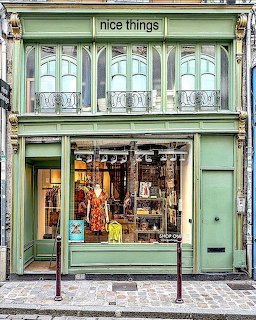 Mint green vintage storefront with ornate balcony and display windows on cobblestone street