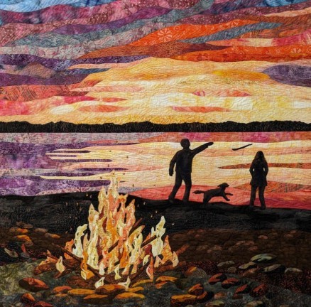 Fabric quilt art showing two people and dog silhouettes by campfire at colorful sunset beach