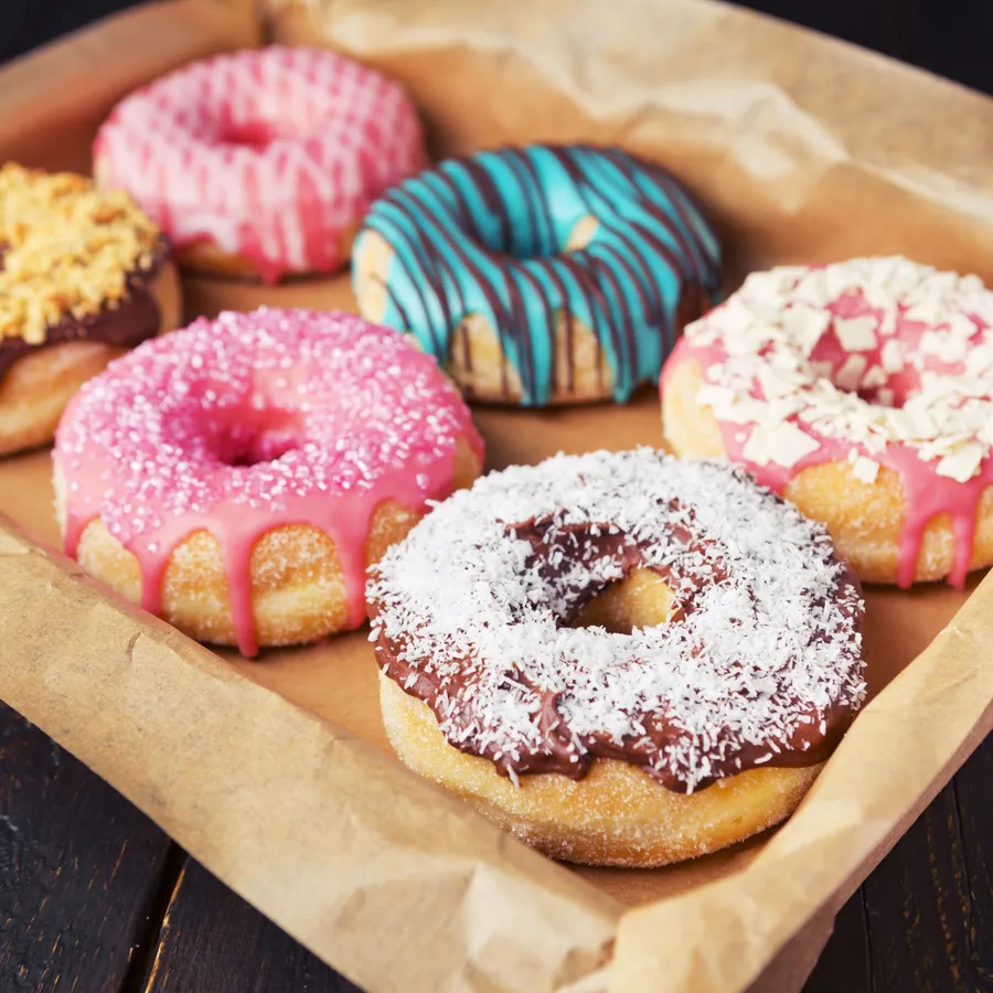 Assorted iced donuts with sprinkles on brown paper on a wooden table