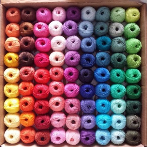 Colorful yarn balls arranged in neat rows by rainbow shades in a wooden tray