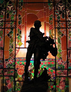 Silhouette of a statue in front of colorful Art Nouveau stained glass windows with geometric patterns