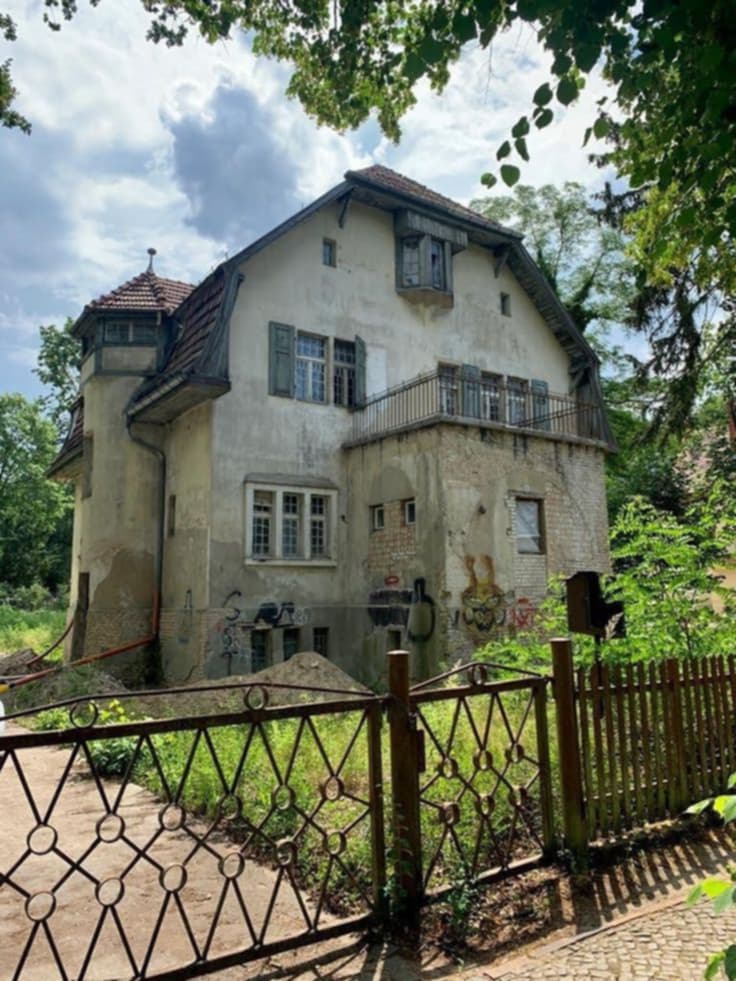 Weathered old European villa with turret and wooden fence surrounded by green trees