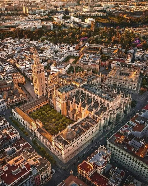 Aerial photograph of Seville Cathedral complex surrounded by city buildings at sunset