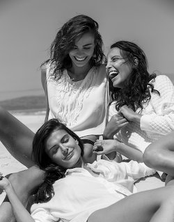 Black and white photo of three smiling women laughing together on a beach