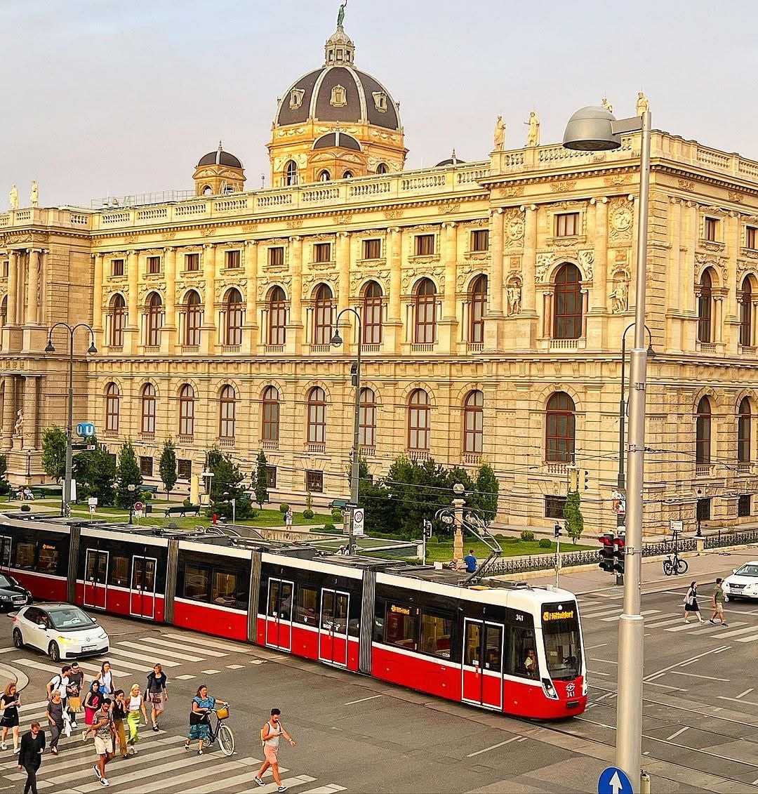 Grand Baroque museum building in Vienna with characteristic dome and red vintage tram in foreground