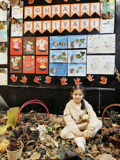Young girl sitting among pine cones and dried leaves in front of autumn-themed classroom display