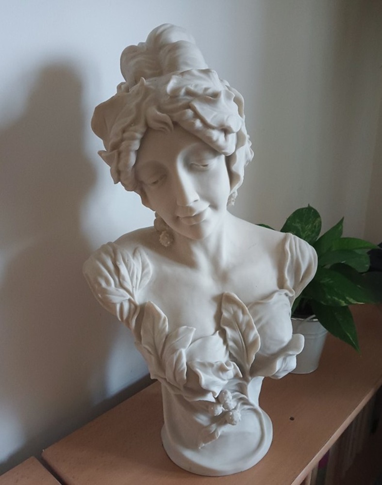 White classical bust sculpture on a wooden shelf beside green leaves