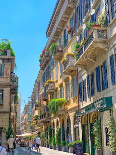 Sunny street in Milan Italy with historic buildings, green balcony plants, and pedestrians walking