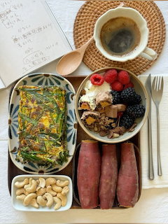 Korean meal tray with rice bowl, side dishes, sausages, nuts, and coffee on woven mat