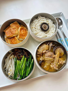Korean meal tray with noodles, soup, vegetables, beef, and fried tofu in round metal bowls