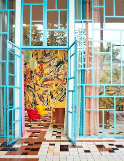 Turquoise hallway with checkered tile floor, glass doors, and yellow abstract painting on wall
