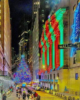 Wall Street sign and NYC skyscrapers lit with red and green neon lights alongside a bright Christmas tree at night