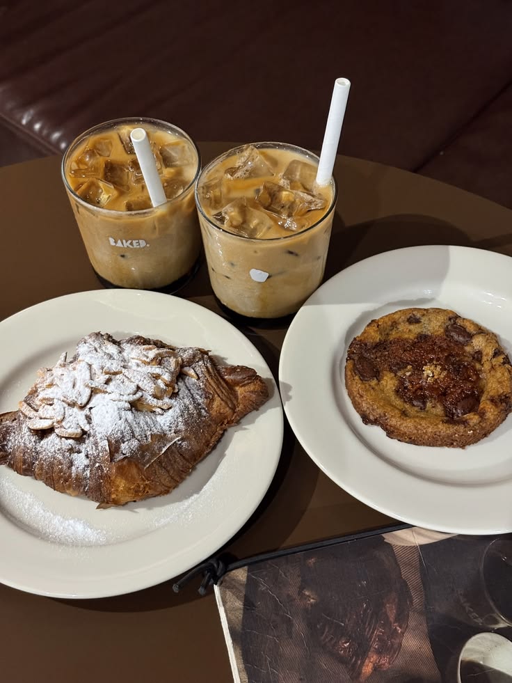 Two iced coffee drinks with pastries including a powdered sugar croissant and a cookie on white plates