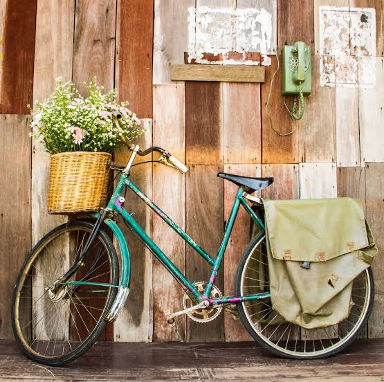 Turquoise vintage bicycle with flower basket against rustic wooden wall