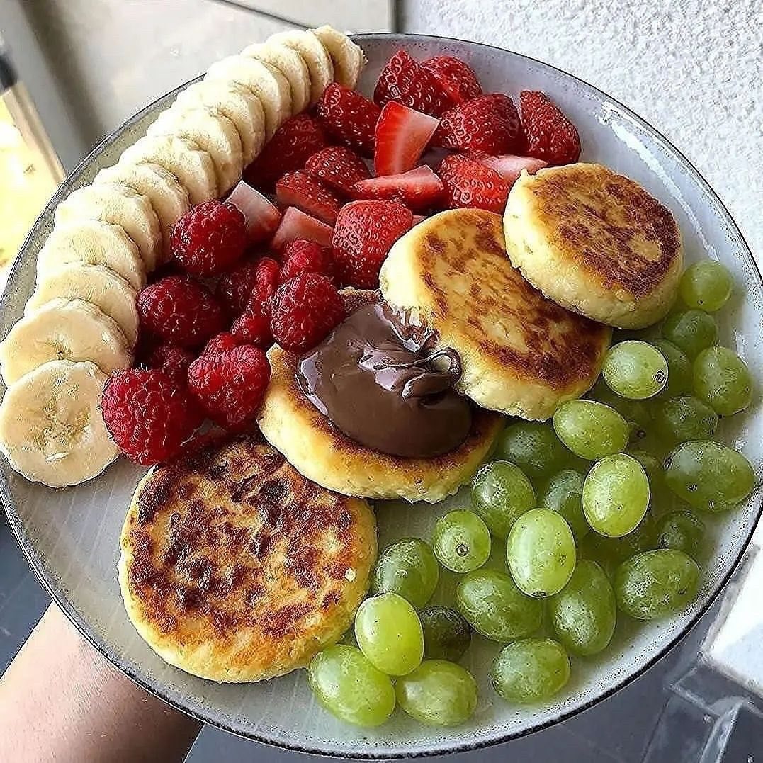 Plate with banana, strawberries, raspberries, green grapes, and small pancakes with chocolate spread