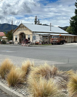 Old station-style building by a road with dry grasses and mountains in the background