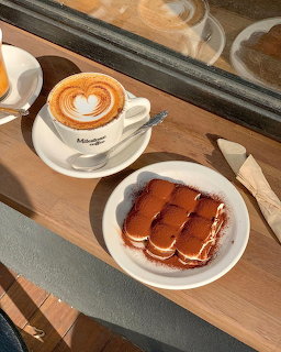 Cappuccino with heart latte art and tiramisu dessert on café table by window