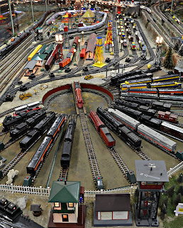 Aerial view of detailed model train layout with roundhouse, locomotives, freight cars, and multiple track lines
