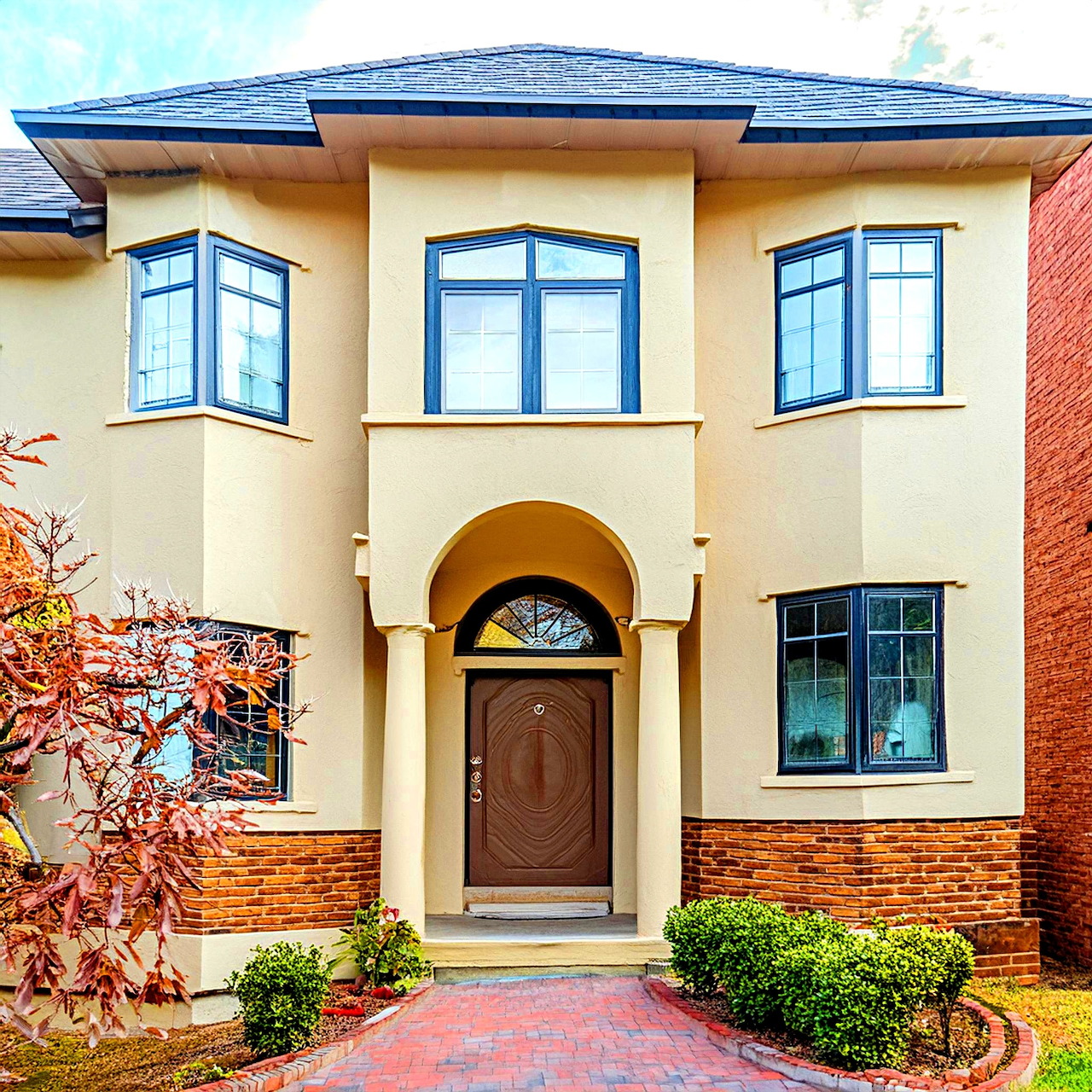 Two-story modern house with cream exterior, blue roof, arched doorway, large windows, and landscaped front yard
