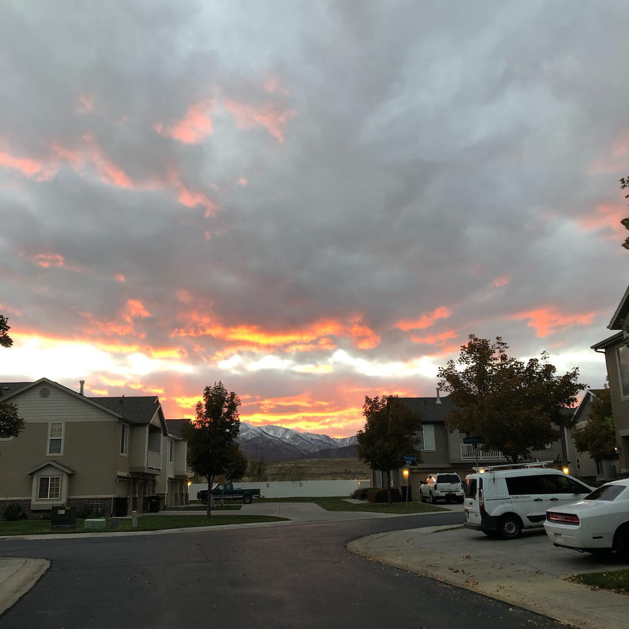Sunset sky over a suburban street with houses, cars, distant mountains, and water