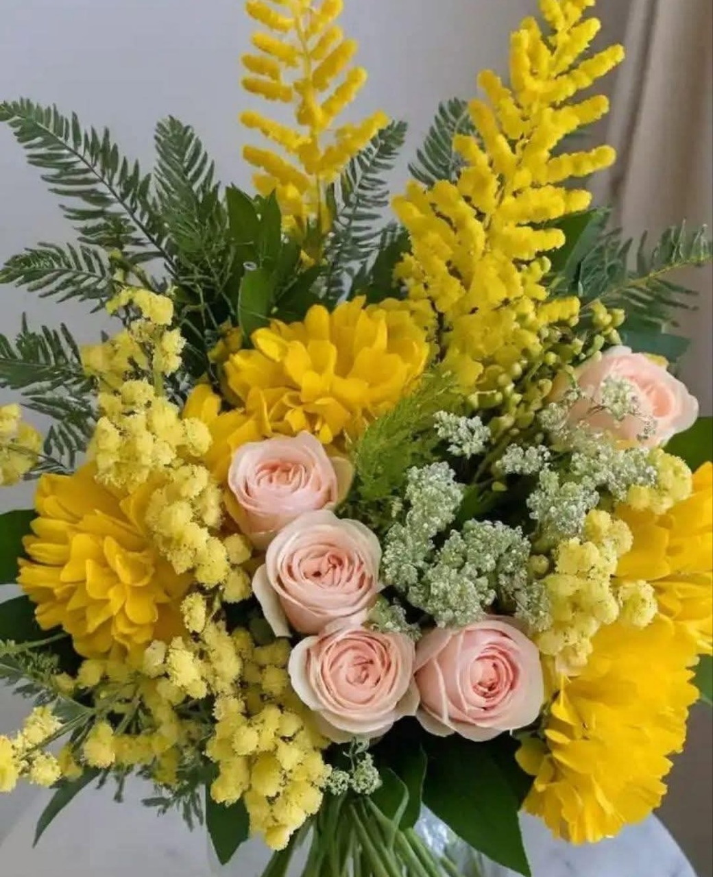 Close-up of a bouquet with yellow flowers, pale pink roses, and green leaves