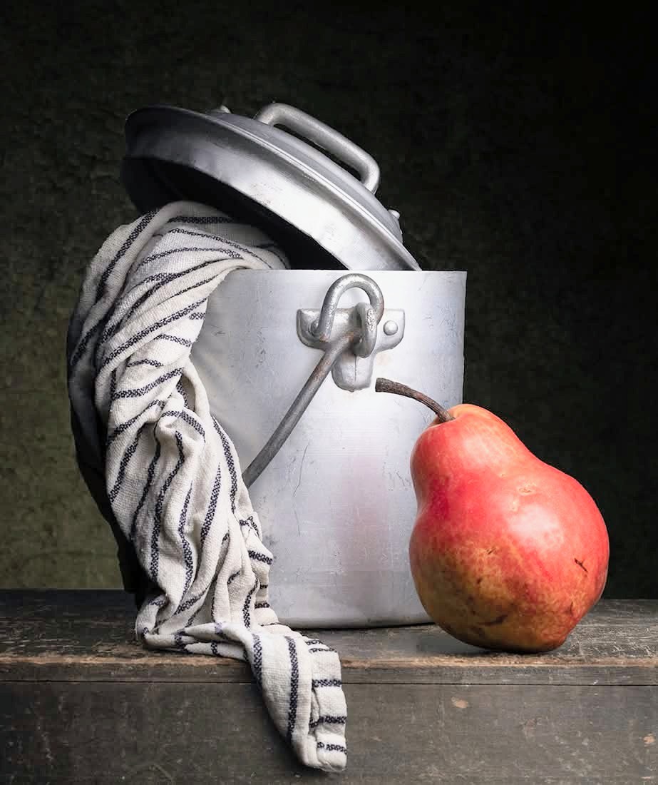 Red pear beside a metal pot and striped cloth on a wooden table
