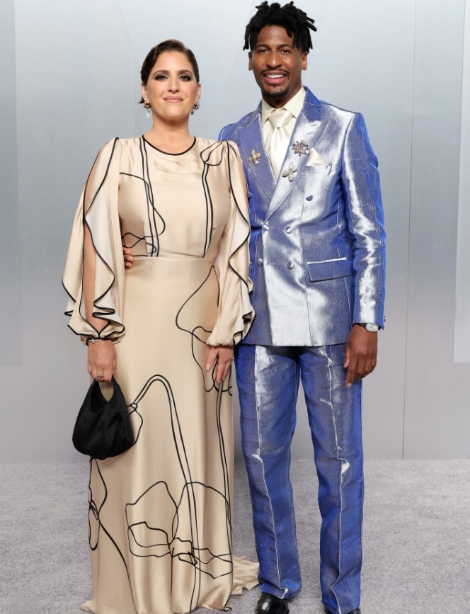 Woman in cream dress with black line drawings standing next to man in shiny blue metalic suit at formal event