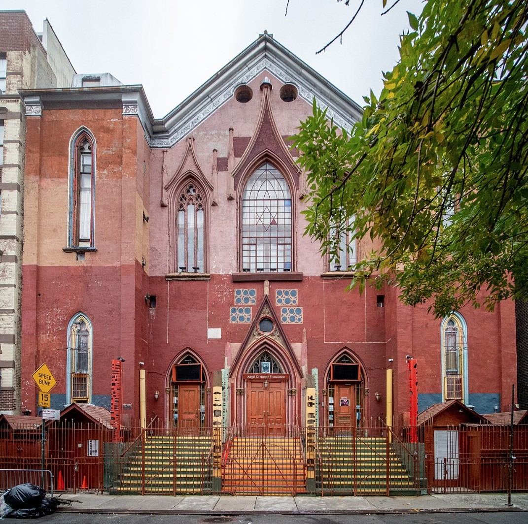 Red brick synagogue building with Gothic arched windows and triple entrance stairways in Manhattan
