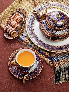 Ornate tea set with blue patterned porcelain, golden tea in cup, teapot, and pastries on decorative plate