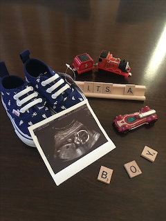Baby boy announcement with blue shoes, ultrasound photo, Scrabble tiles spelling Its A Boy, and toy fire trucks
