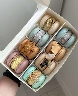 Hand holding an open white box of assorted pastel-colored macarons with decorative toppings