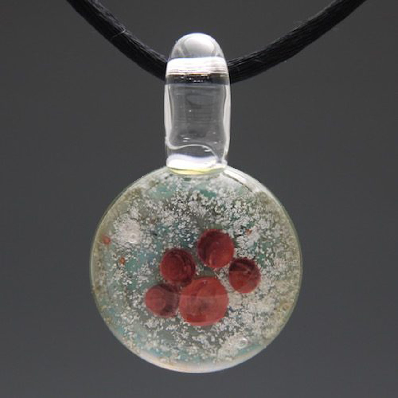Round glass pendant with a red pawprint hanging from a black cord on a gray background