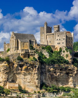 Medieval French castle atop a tall rocky cliff with blue sky and white clouds