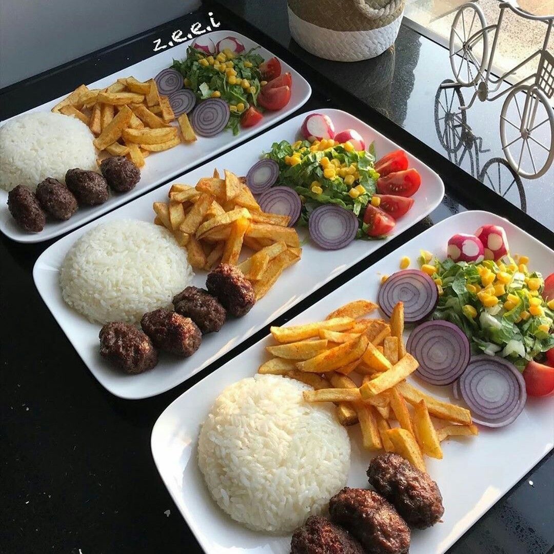 Three identical meal plates with rice, fries, meatballs, salad, tomatoes and onion rings