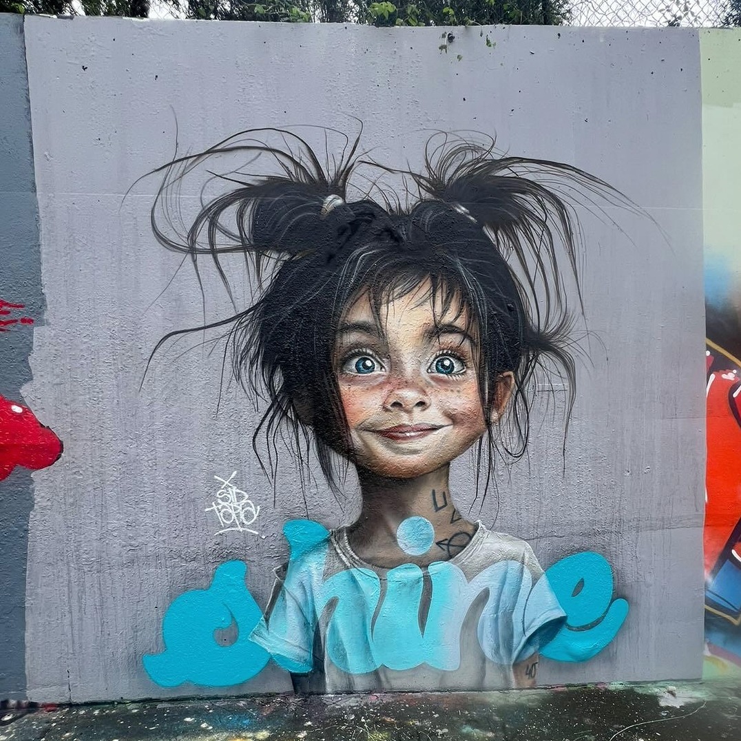 Street art mural of smiling girl with wild black hair wearing turquoise shirt on gray wall