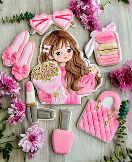 Assortment of pink decorated sugar cookies shaped like fashion items and a girl on a wooden background