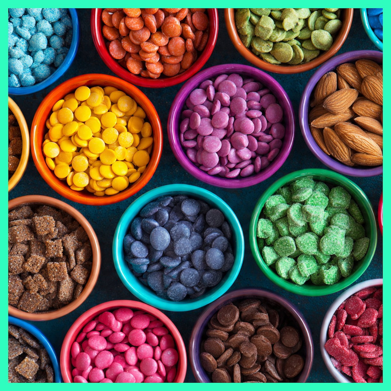 Colorful bowls filled with various candies and snacks arranged in rows from above