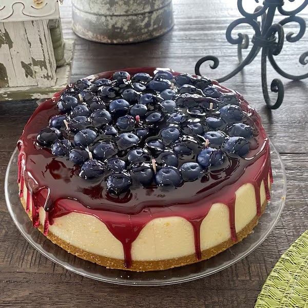 Blueberry-topped cheesecake with red glaze dripping down sides on glass plate