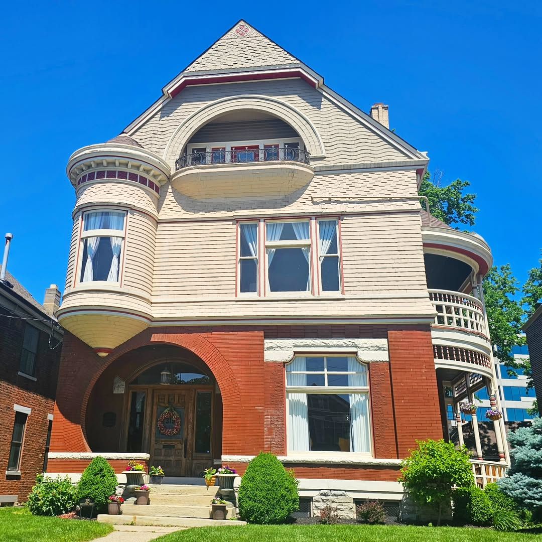 Victorian house with turret, arched windows, and manicured lawn on sunny day