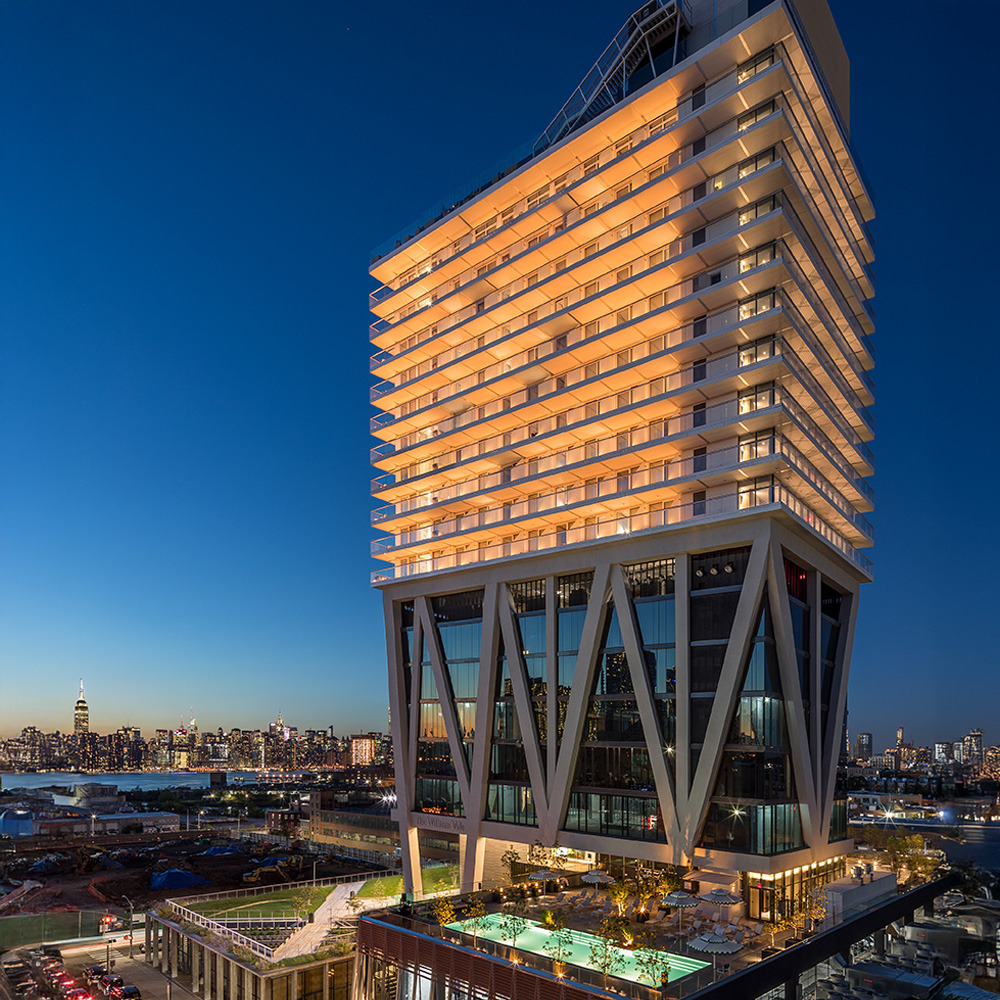 Illuminated William Vale Hotel at night in Brooklyn with city skyline in the background